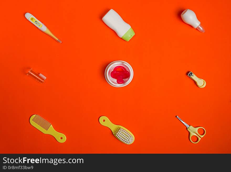 Baby`s accessories on red background, top view. Pacifier, baby nail clipper, hair brush, comb and empty space for logo or text on shower gel, red background, flat lay.