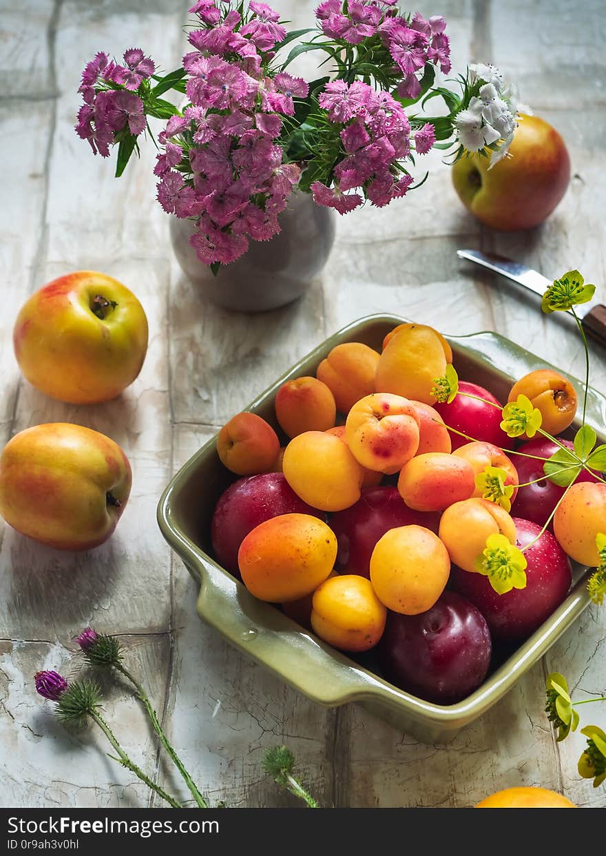 Fruit set of fresh fruits in a ceramic square plate, a bouquet of forest carnations in a small vase