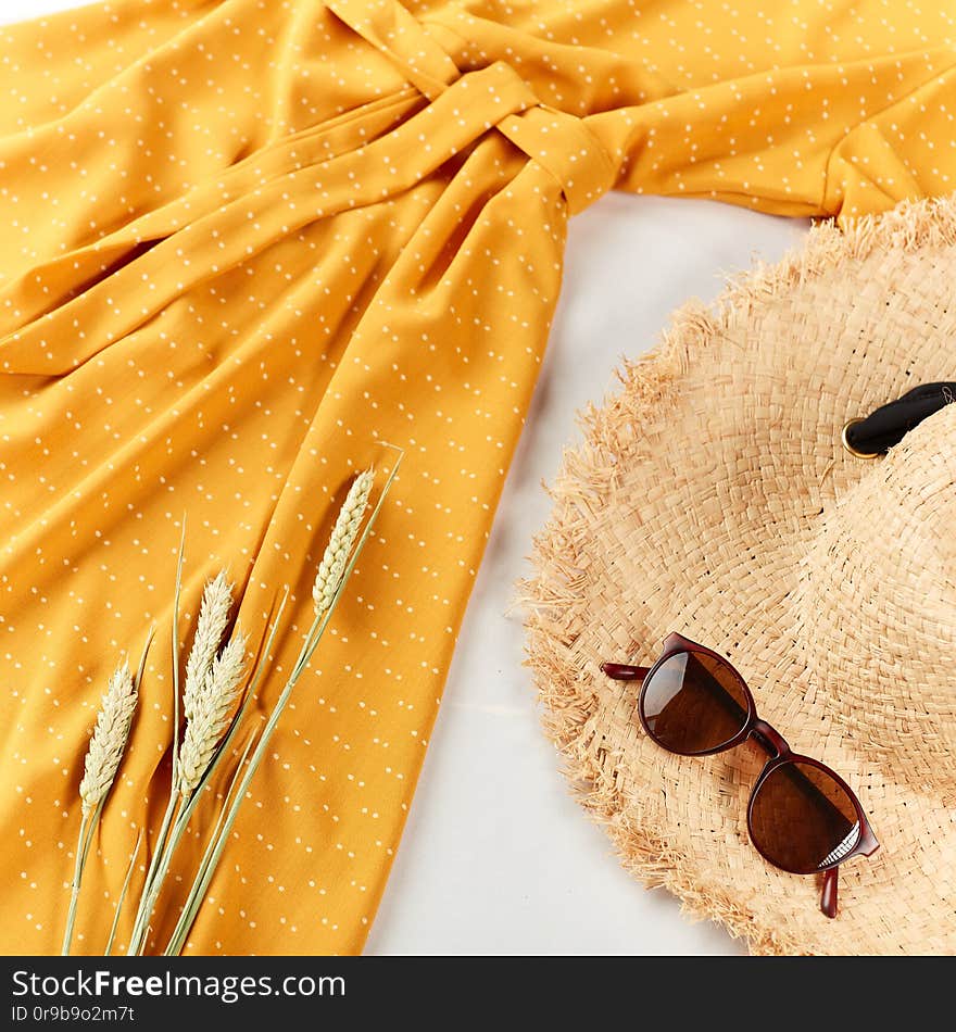 Wheat,straw hat, yellow stylish dress on light white background. Flat lay