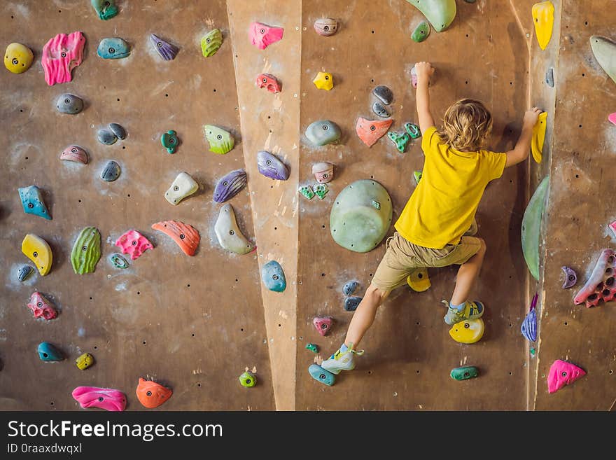 Little boy climbing a rock wall in special boots. indoor.