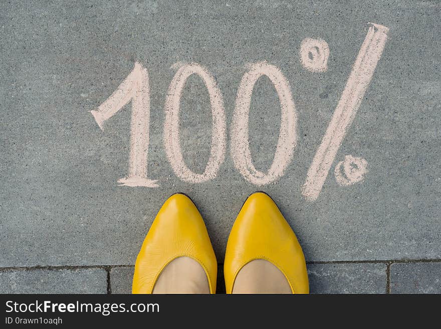 Female feet with text 100 percent written on grey sidewalk