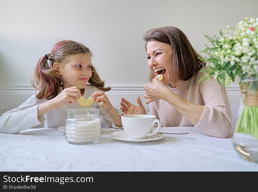 Laughing mother and daughter drinking from cups and eating lemon