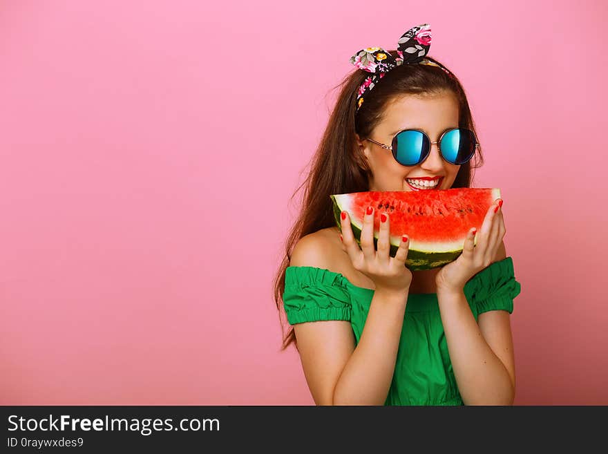 Portrait of a happy girl, holding a slice of watermelon in hand try to bite, over colorful pink background. Copy space.