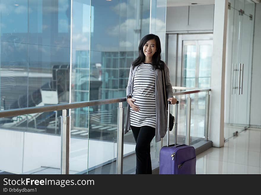 Asian pregnant woman standing pulling suitcase on the airport before flight departure