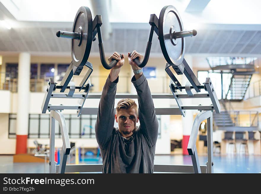 Front view of young fit Caucasian man exercising with shoulder machine in fitness studio. Bright modern gym with fit healthy people working out and training