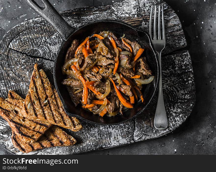 Slow cooker braised beef with onions and carrots in a pan on a dark background, top view