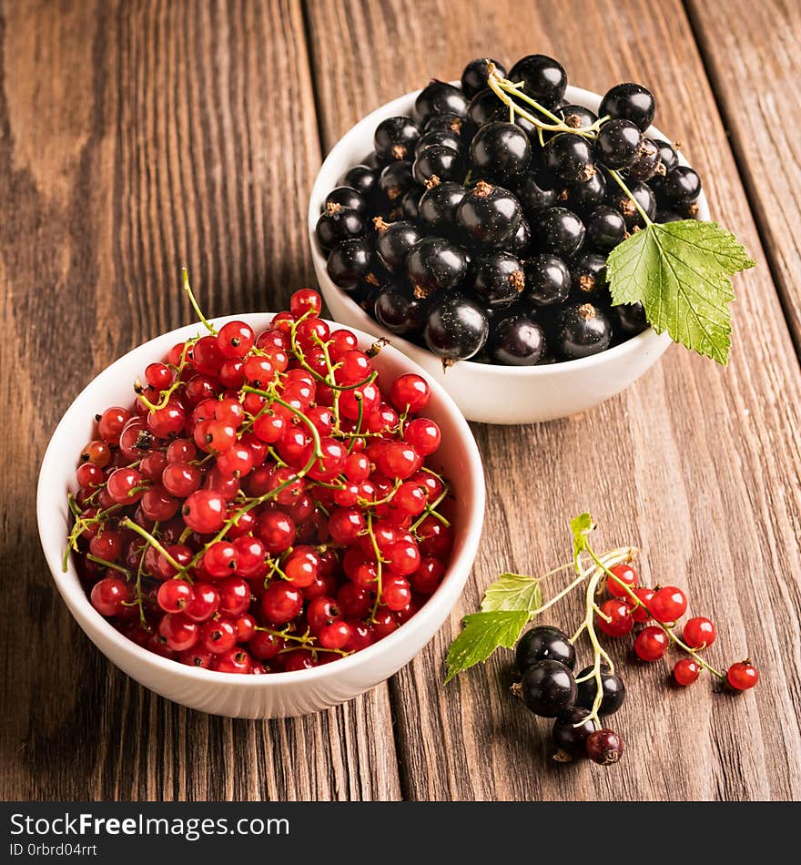 Fresh ripe red black currant berry in white bowls on wooden background. Square frame