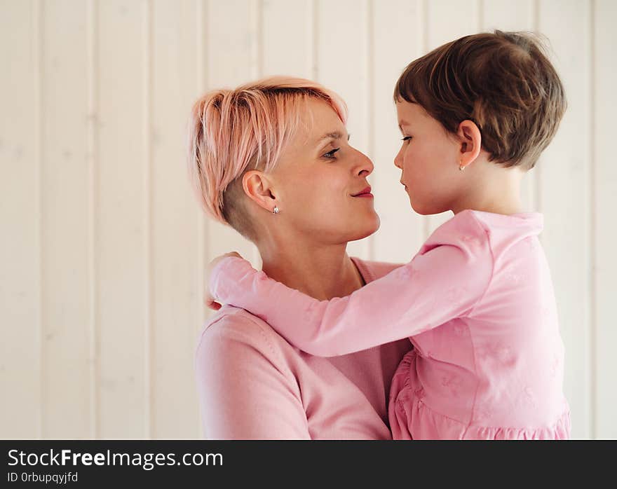 A young woman with small daughter, white wooden wall in the background.