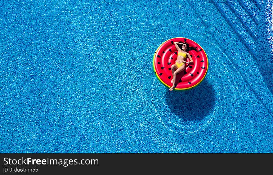 Young woman relaxing on watermelon in hotel resort pool. Top view of rich girl floating with fruit mattress drinking cocktail.