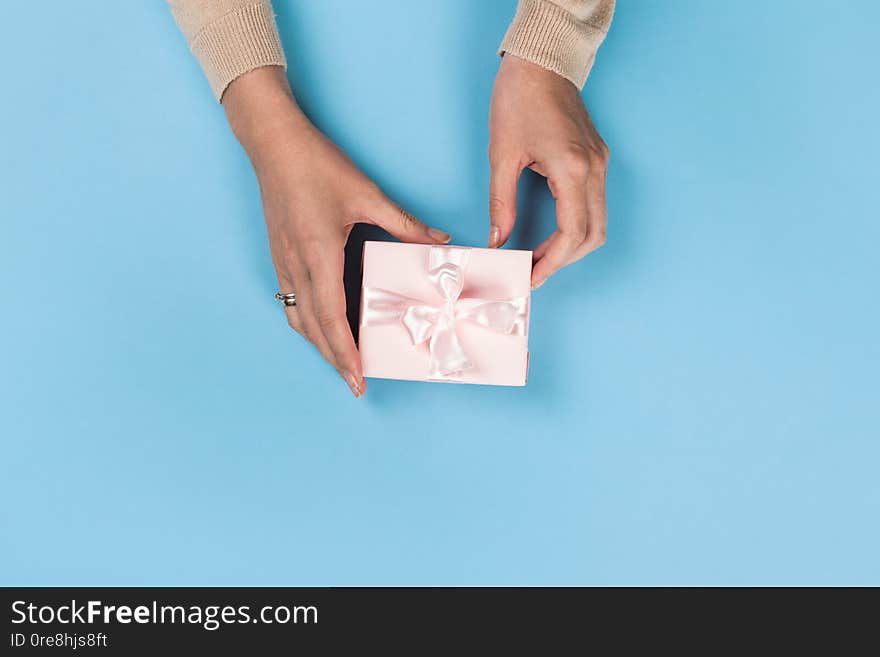 Womans hands holding gift or present box on blue pastel table top view. Flat lay  for birthday or New Year