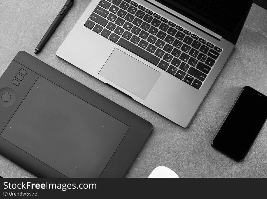 Workplace with open laptop with black screen, mouse, graphics tablet and smart phone on modern grey stone desk, angled notebook on