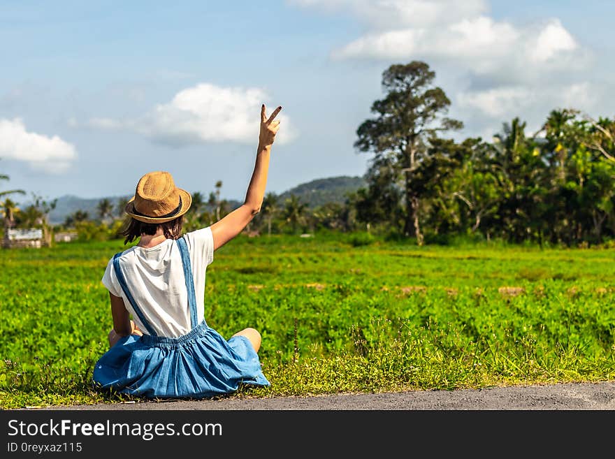 Tropical portrait of young happy woman with straw hat on a road with coconut palms and tropical trees. Bali island. Indonesia.