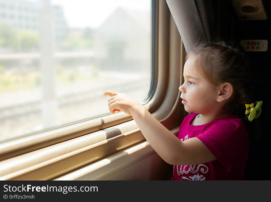 Happy little girl traveling by train. She is lokking through the window