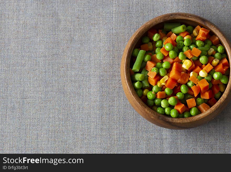 Mixed vegetables, with carrot, beans, peas and sweet corn,  in a wooden bowl.  On a grey tablecloth