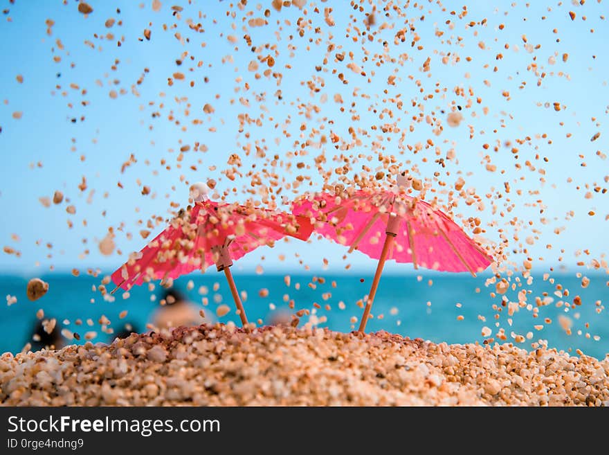 Two red coctail umbrellas under sand rain. Blue sea and sky at the background. Resort background