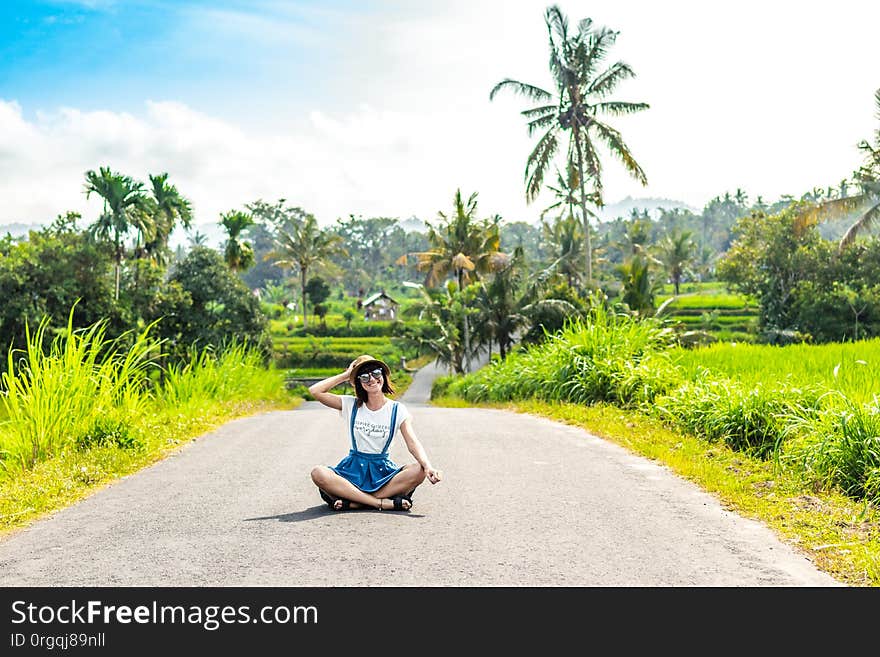 Tropical portrait of young happy woman with straw hat on a road with coconut palms and tropical trees. Bali island. Indonesia.