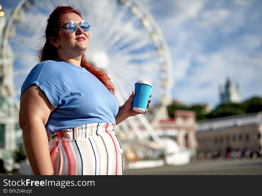 Happy young and fat woman smiling, holding cup with coffee, standing on city street. Happy young and fat woman smiling, holding cup with coffee, standing on city street
