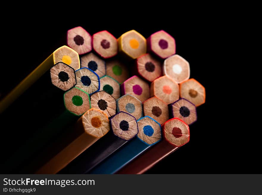 Wooden pencils in all colors seen at the base of pencils. Colored pencils stacked. With a black background.Colors. Back to school