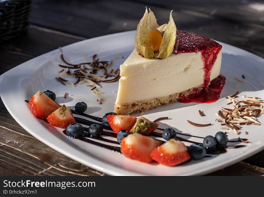 Classic cheesecake with raspberry jam on a plate decorated with fresh strawberries.