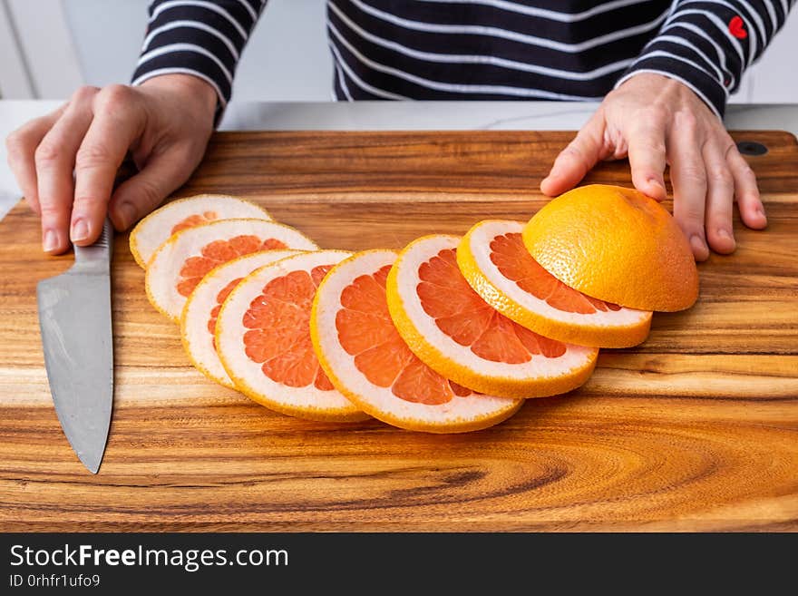 Caucasian woman hands placed on wooden chopping board with sliced red grapefruit and knife. Caucasian woman hands placed on wooden chopping board with sliced red grapefruit and knife