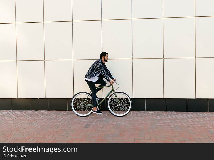 Side view of a stylish bearded man riding a bicycle on the city street. Side view of a stylish bearded man riding a bicycle on the city street