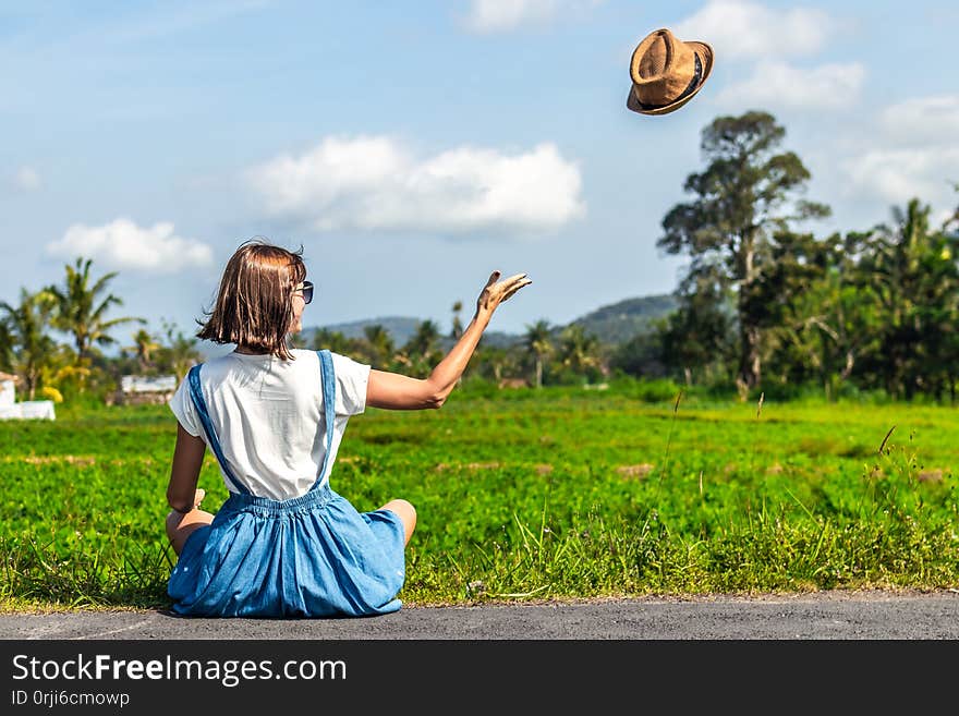 Tropical portrait of young happy woman with straw hat on a road with coconut palms and tropical trees. Bali island. Indonesia.