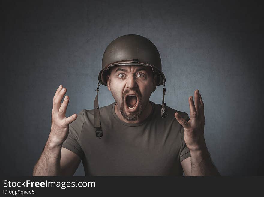 Portrait of a screaming soldier with open arms. He is wearing a metal helmet