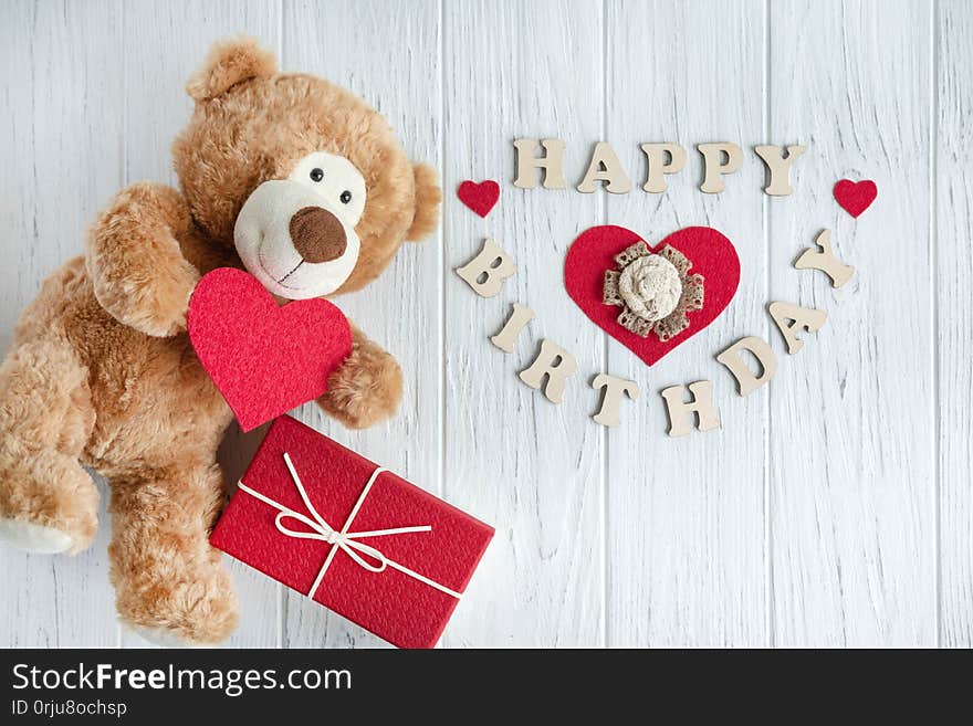 Toy bear with a heart and boxes with gifts on a light wooden background. The design of the birthday greeting card. Frame for the