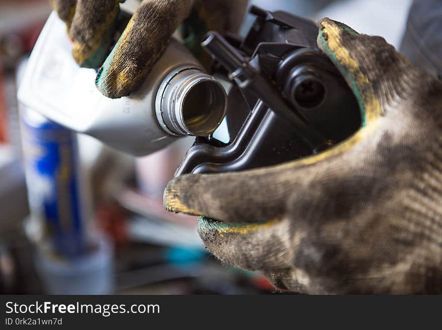 A mechanic in dirty gloves and overalls pours engine oil from a canister into the engine. The process of working in a service station.