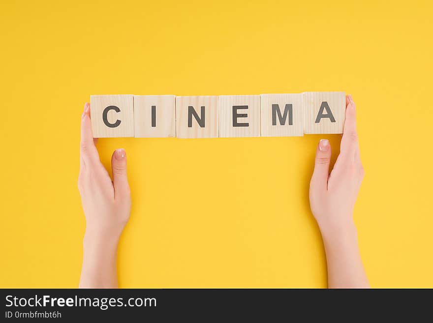 Top view of hands holding wooden cubes with cinema lettering isolated on yellow