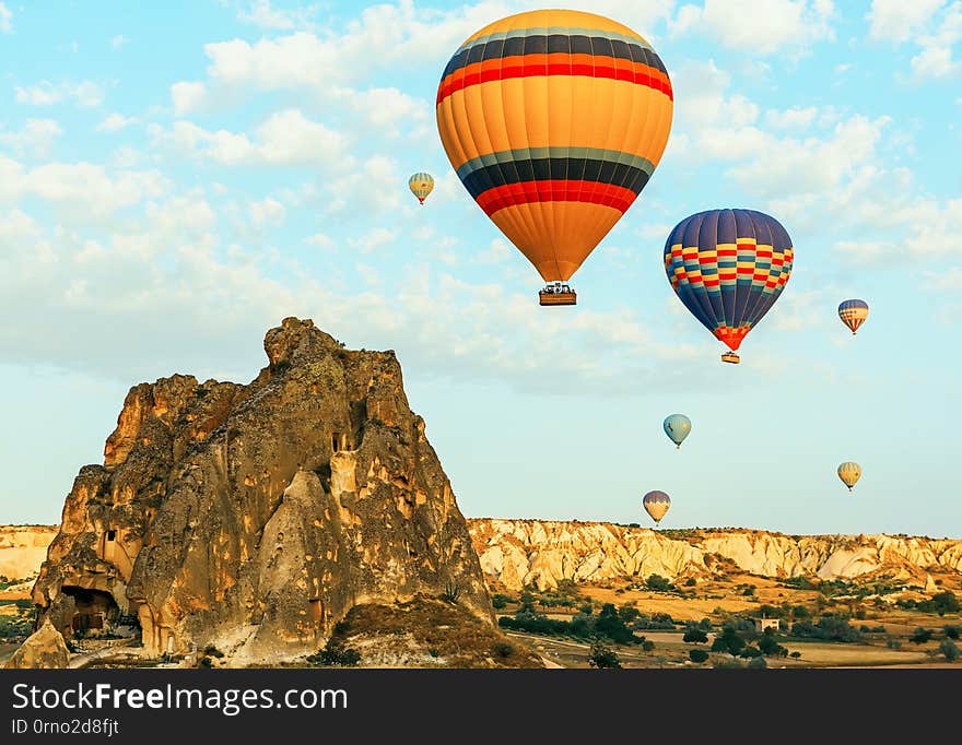 Colorful air balloons fly up into the sky at sunrise among a beautiful rocky landscape.