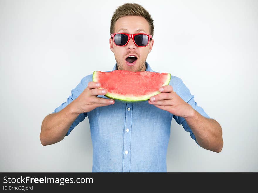 Young handsome man in red eyeglasses biting watermelon on isolated white background.