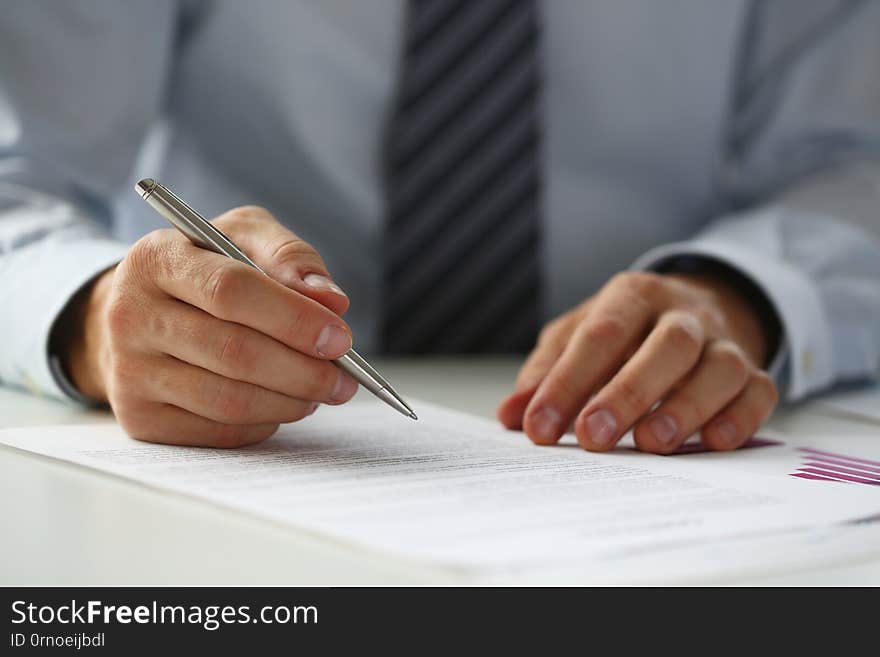 Hand of businessman in suit filling and signing with silver pen partnership agreement form clipped to pad closeup. Management training course, some important document, team leader ambition concept