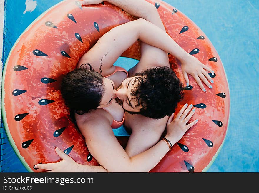 Top View Of Young Couple In Love Kissing And Hugging On Watermelon Lilo In Swimming Pool At Resort. Summer Vacation Concept. Love