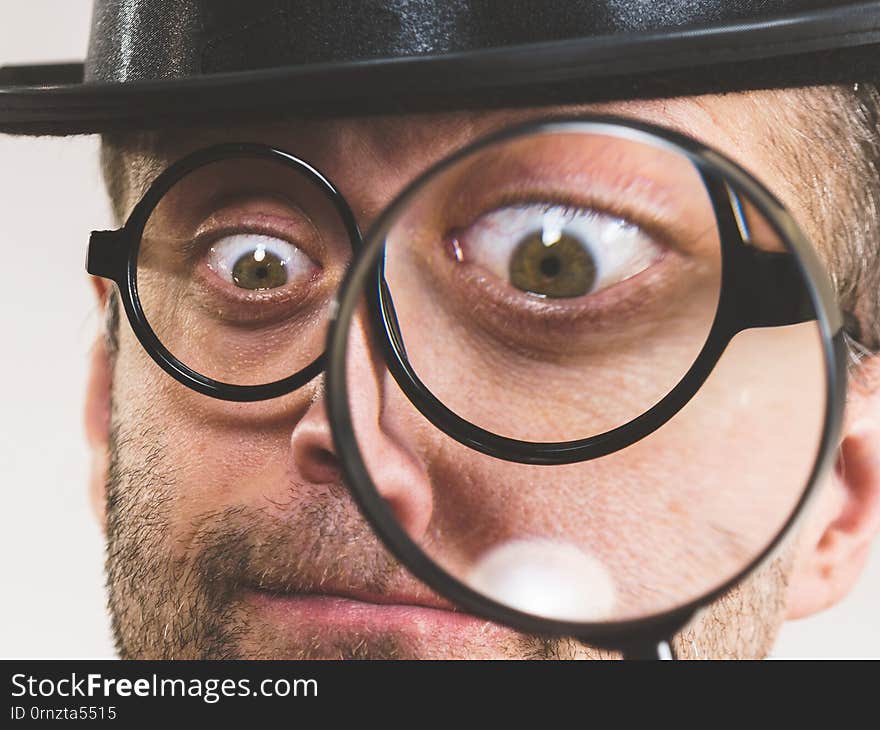 Funny adult guy wearig weird eyeglasses investigating something using magnifying glass making his eye looking big. Funny adult guy wearig weird eyeglasses investigating something using magnifying glass making his eye looking big