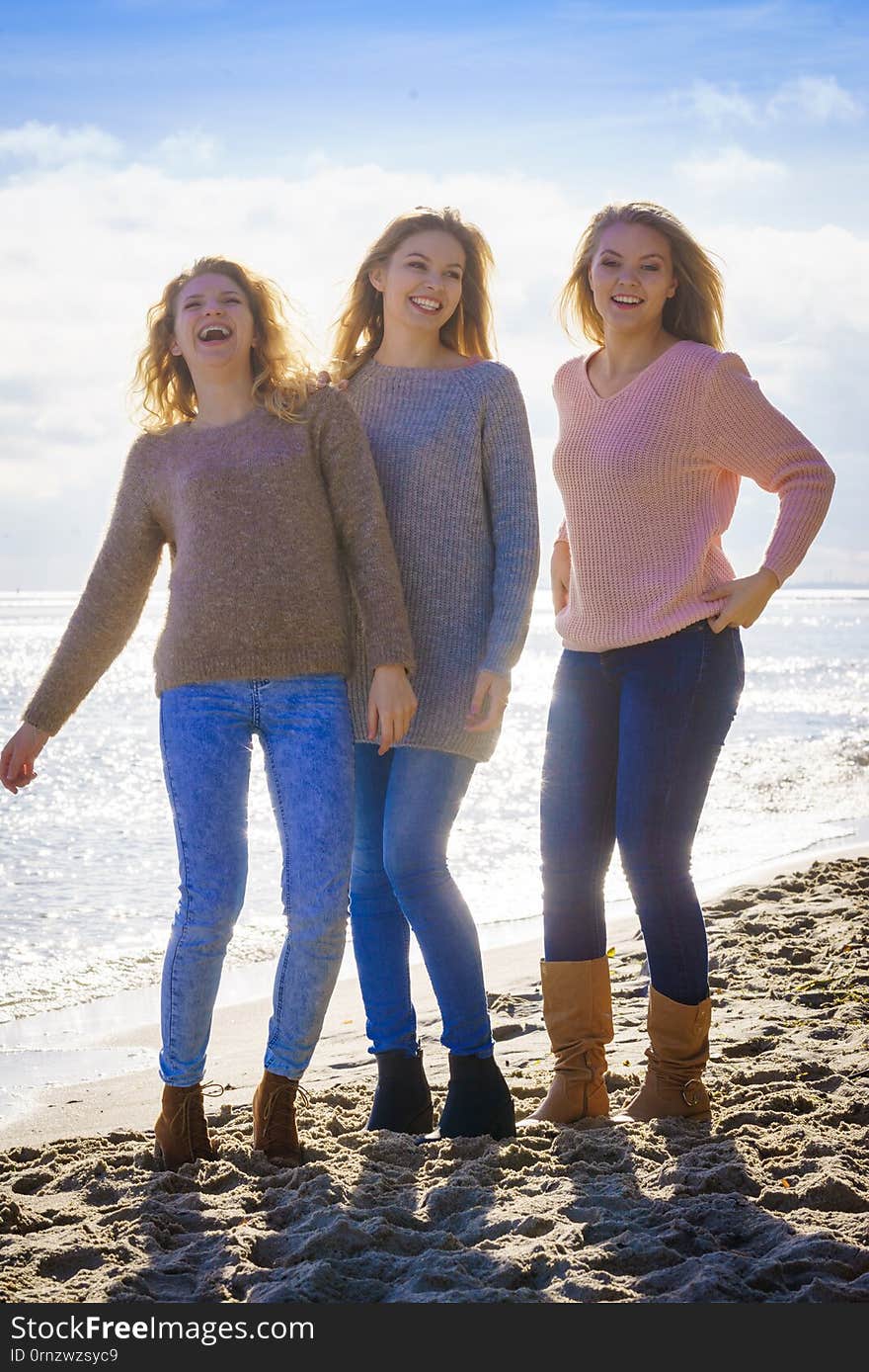 Three fashionable women wearing sweaters during warm autumnal weather spending their free time on sunny beach. Fashion models outdoor. Three fashionable women wearing sweaters during warm autumnal weather spending their free time on sunny beach. Fashion models outdoor