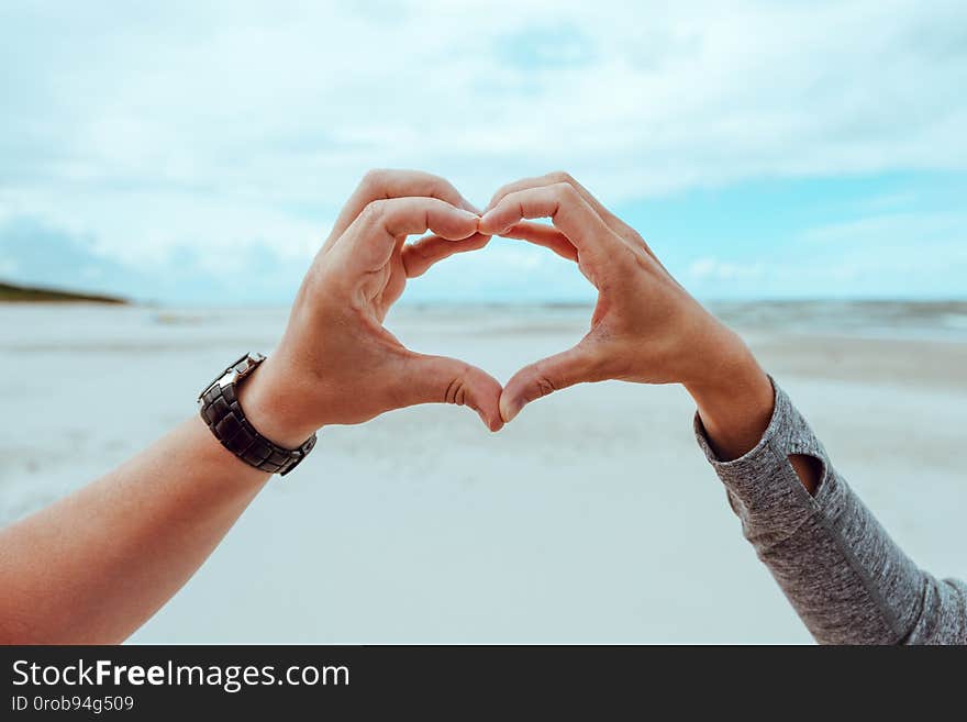 Hands of a woman and a man forming a heart shape against a cloudy summer sky