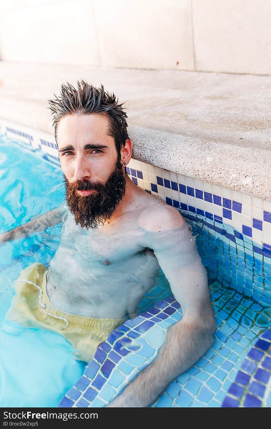 Portrait of a relaxed young man with a beard sitting in the pool. Holiday concept