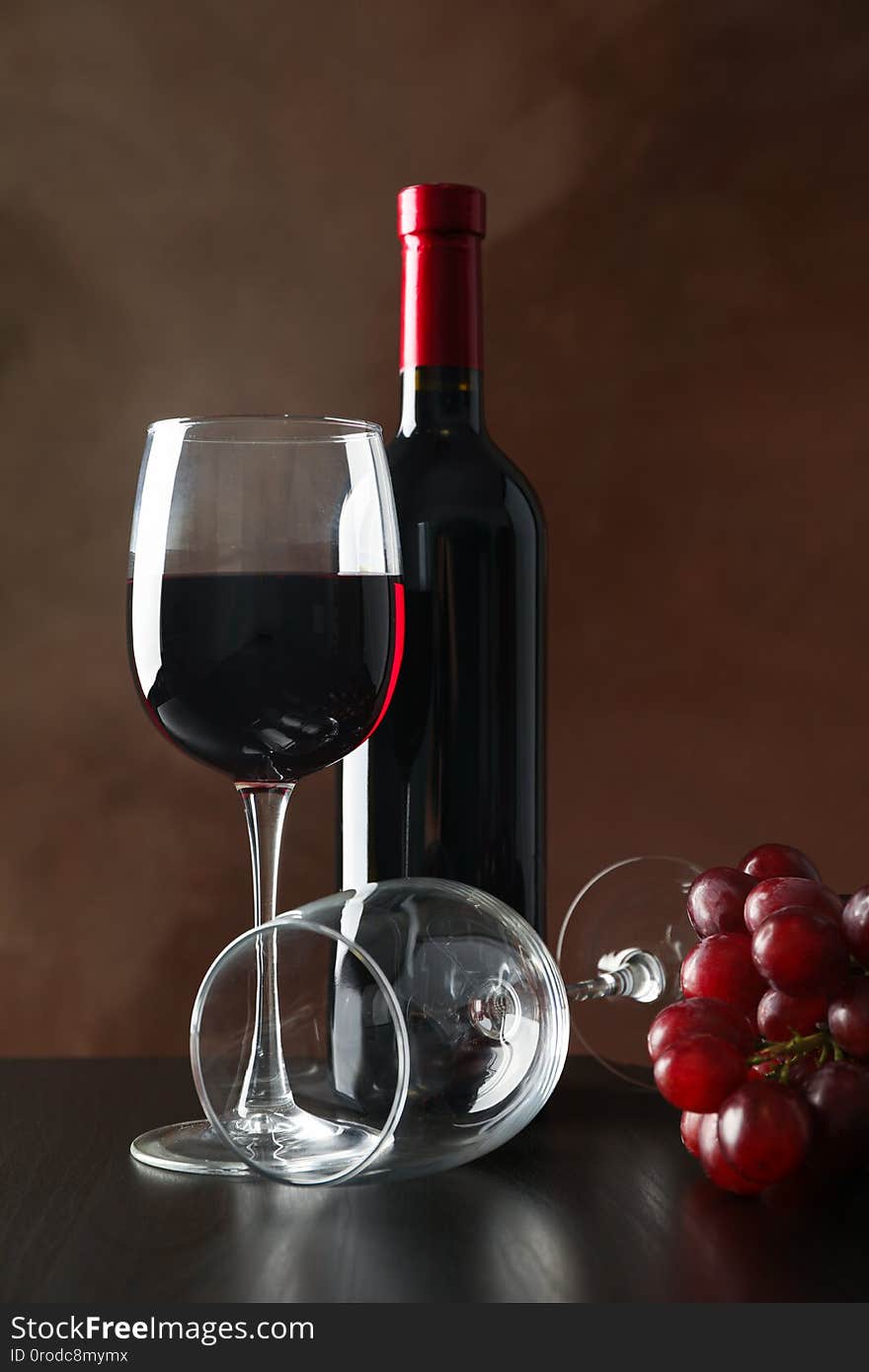 Grapes, bottle and glass with wine against brown background, copy space