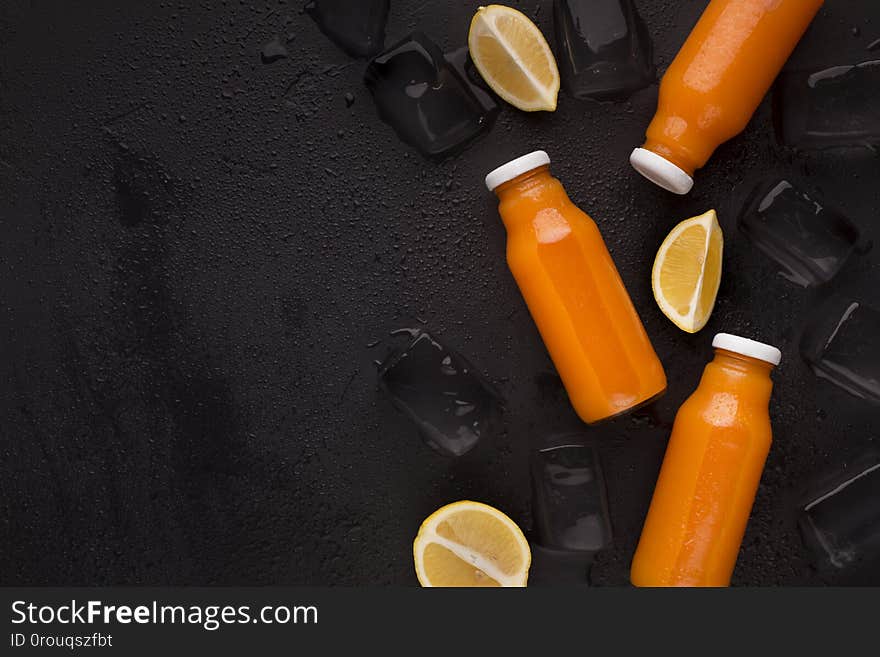 Orange fresh blended detox cocktail on black background with lemon slices and ice cubes