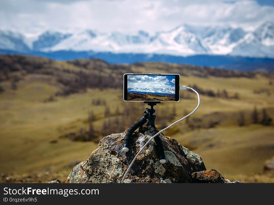 Smartphone on tripod mounted on stone in front of  stunning view of the snow-capped peaks. Image is focused on display