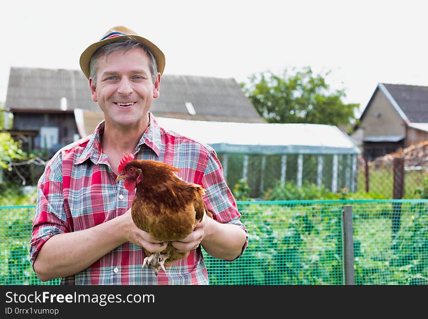 Photo of Mature farmer wearing hat while carrying chicken against barn