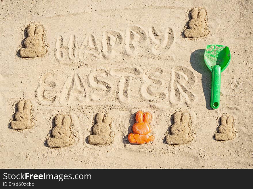 Text Happy Easter and several Easter bunnieas are on the sand. Text Happy Easter and several Easter bunnieas are on the sand