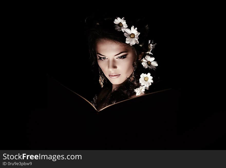 Girl with chamomile reading magic book with mystic light