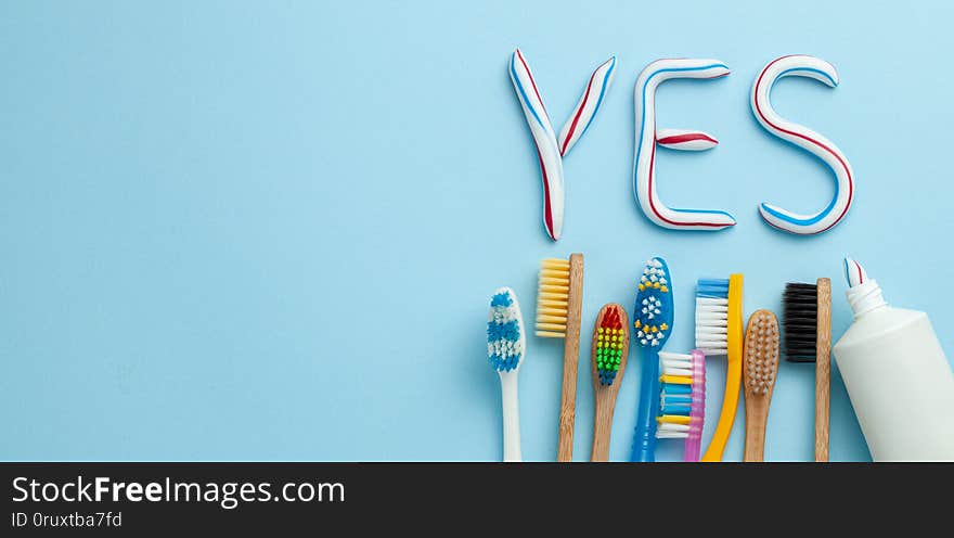 Word YES from toothpaste. Tube of colored toothpaste and toothbrush on blue background. The concept of proper cleaning and care of teeth. Copy space for text