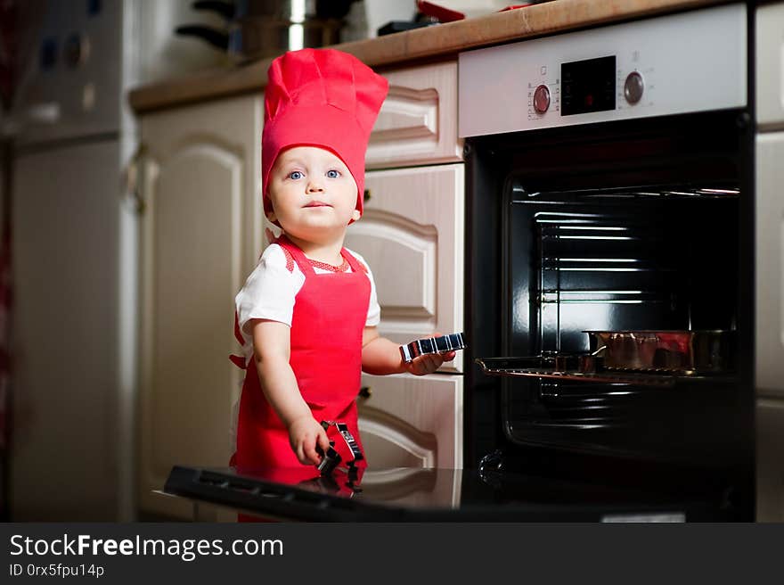 Little girl in a red cook suit plays with kitchen utensils near the oven. Playing in the kitchen close up