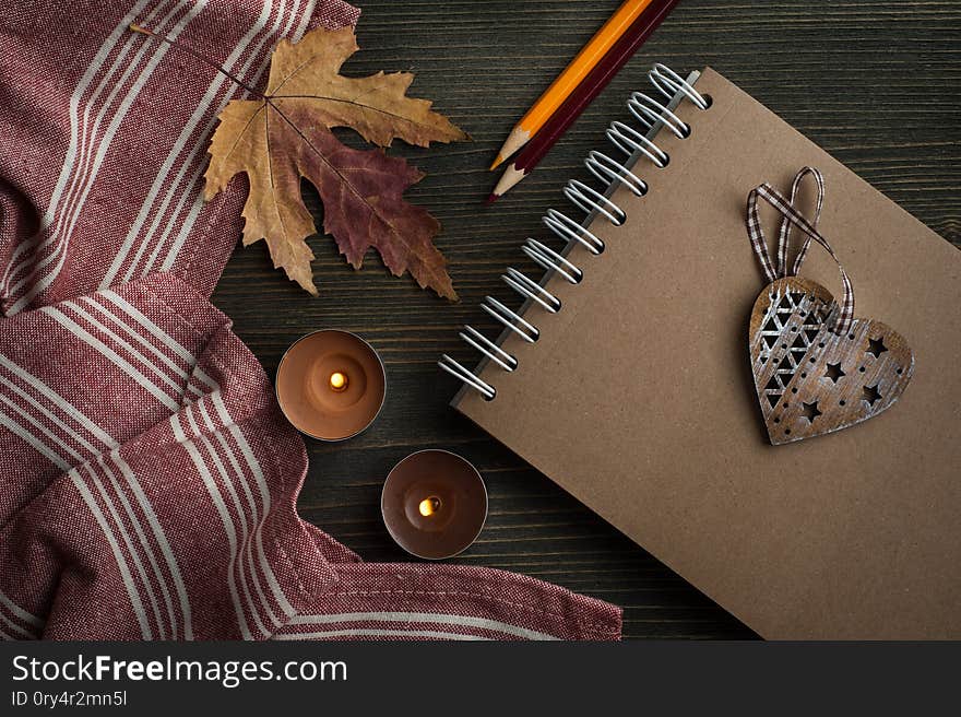Dark wooden background with autumnal leaves and lit candles, top view with copy space