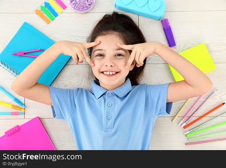 Cute little girl with school stationery on wooden background, top view