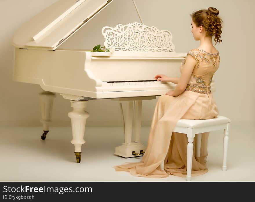 A teenage girl is playing on a white grand piano. The concept of creative development of personality, music education.