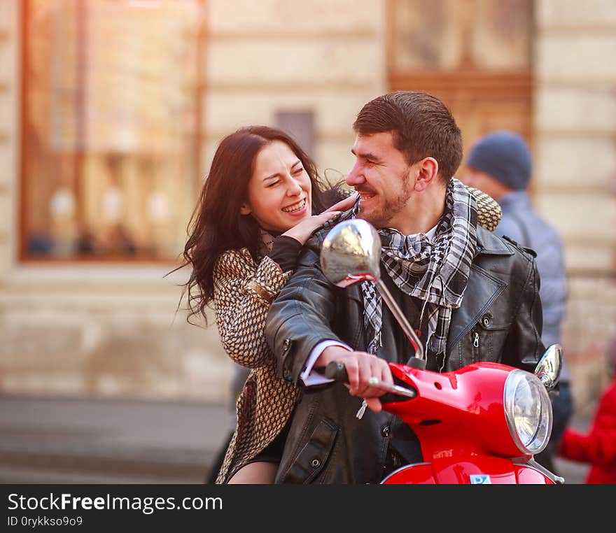 Happy young couple riding a scooter bike in the autumn city together. Happy young couple riding a scooter bike in the autumn city together